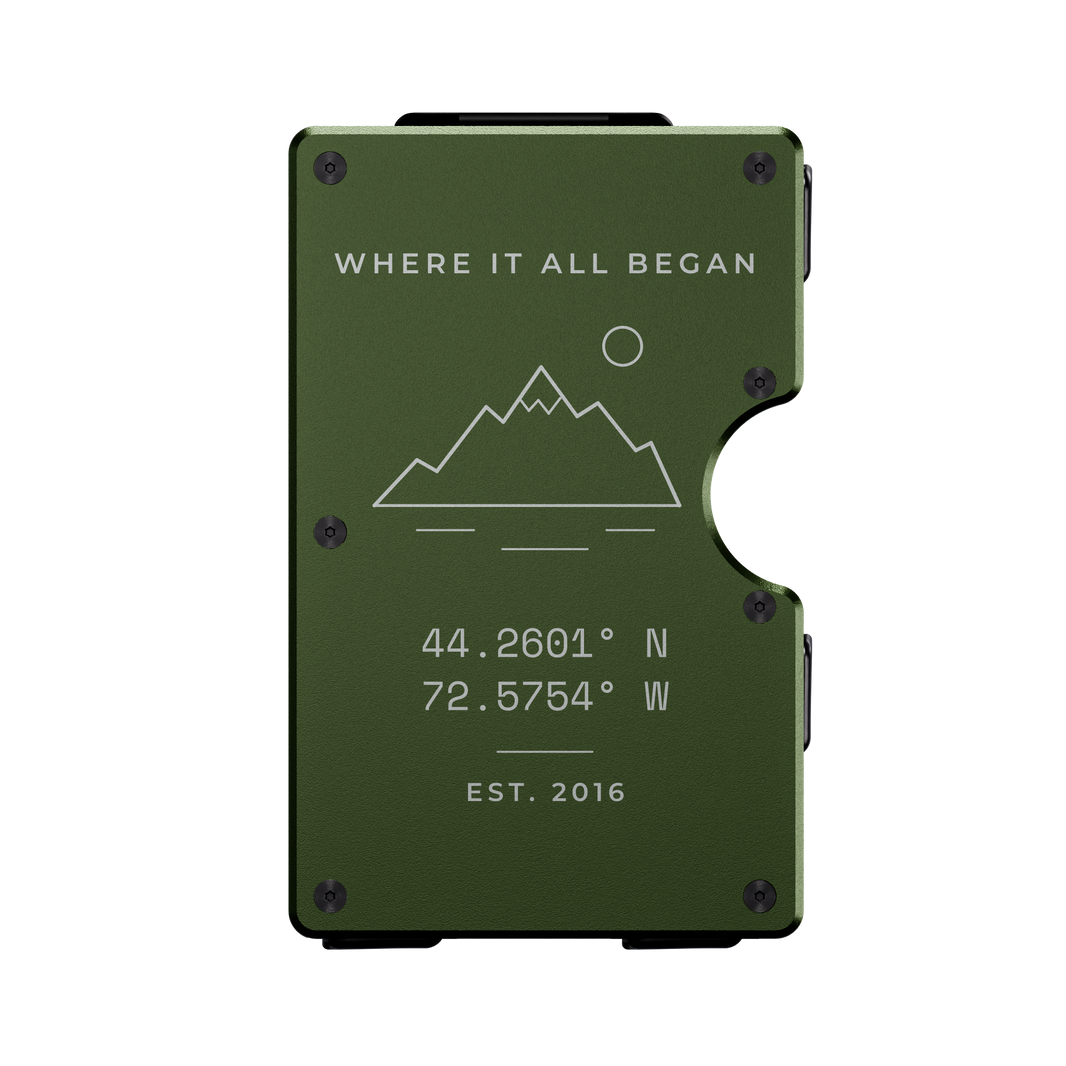 Project 1-of-1 personalized metal wallet in Verde Selva green, laser-engraved with coordinates and a mountain scene (example design)